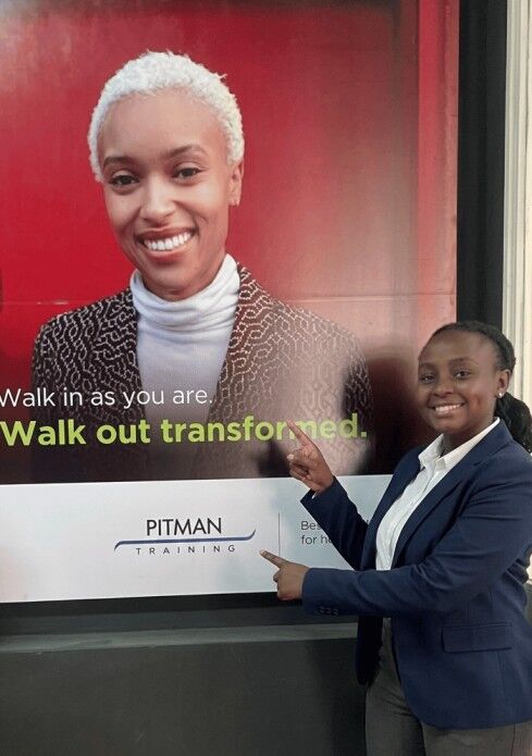 Cindy Nasimiyu Ndirangu - Professional Development Diploma Success Story Cindy Nasimiyu Ndirangu, Pitman Training Kenya Professional Development Diploma graduate, pointing at a Pitman Training poster